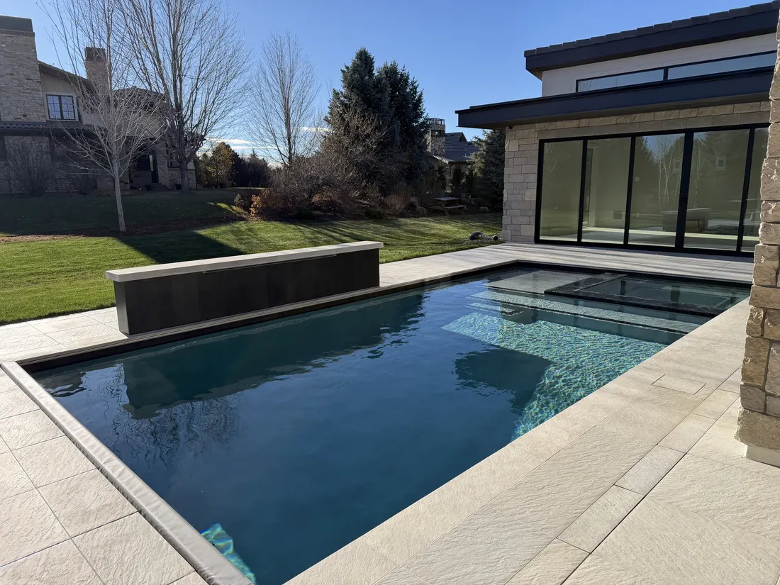 Dark-bottom pool with a raised spa and spillway beside a contemporary stone residence