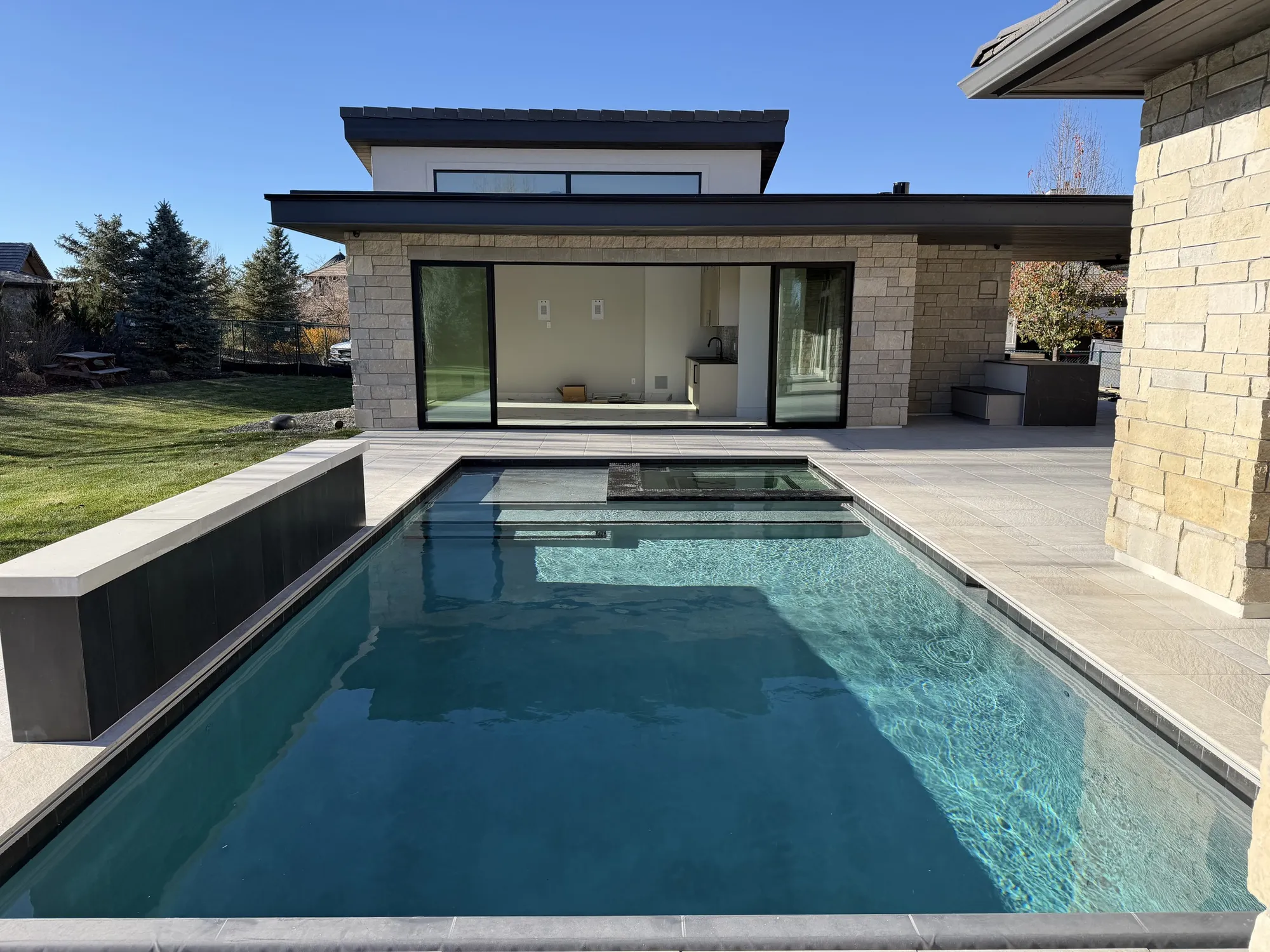 Dark-bottom pool and stone terrace beside a contemporary stone residence