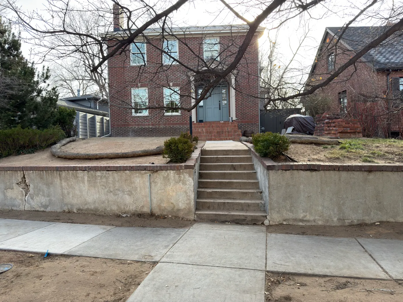 The front garden before work — a cracked, spalling concrete retaining wall and plain concrete steps holding back bare ground