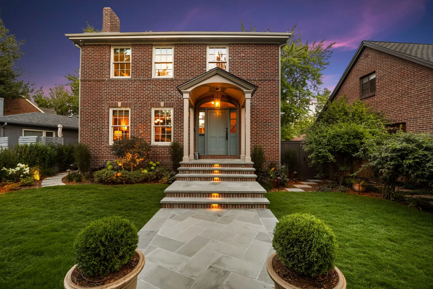 Brick colonial at twilight with a lit entry walk and layered planting