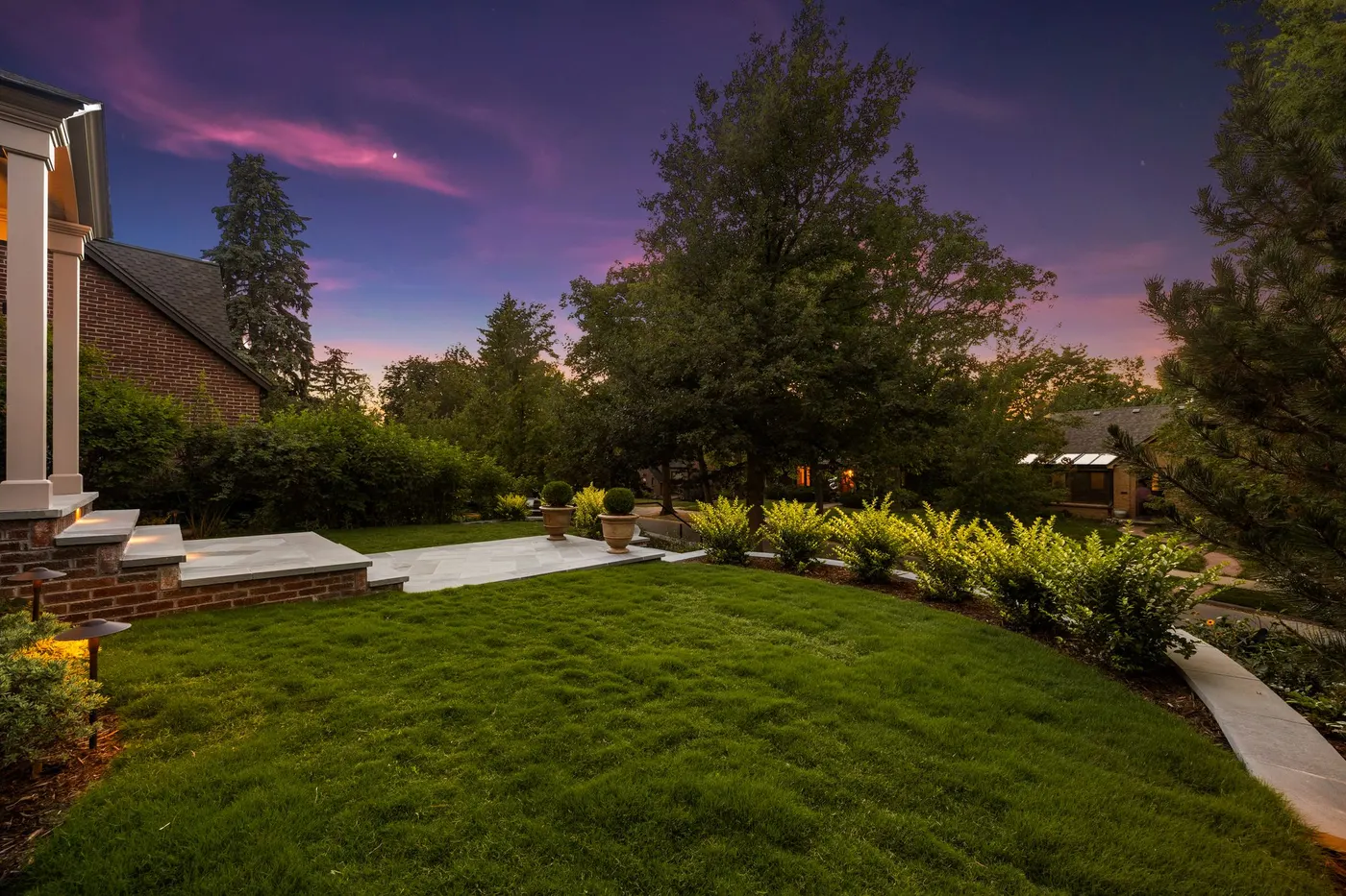 Lit lawn and beds under a twilight sky