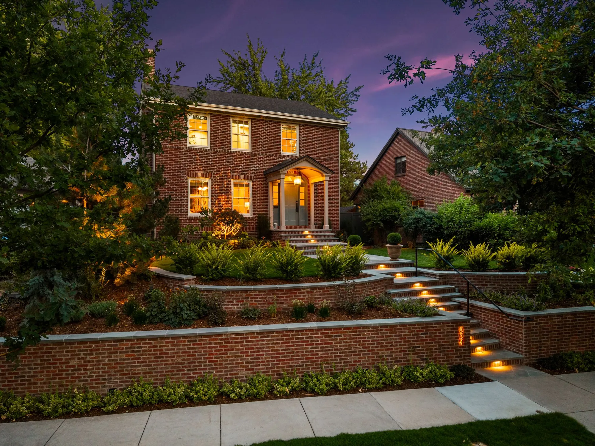 Brick colonial at twilight with terraced garden walls and illuminated steps
